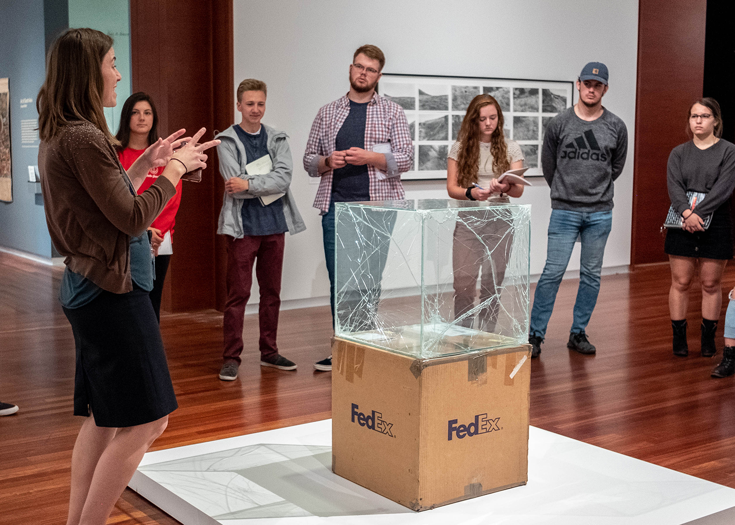 Whitney Tassie discuss a sculpture of a large cracked glass box with a group of University students