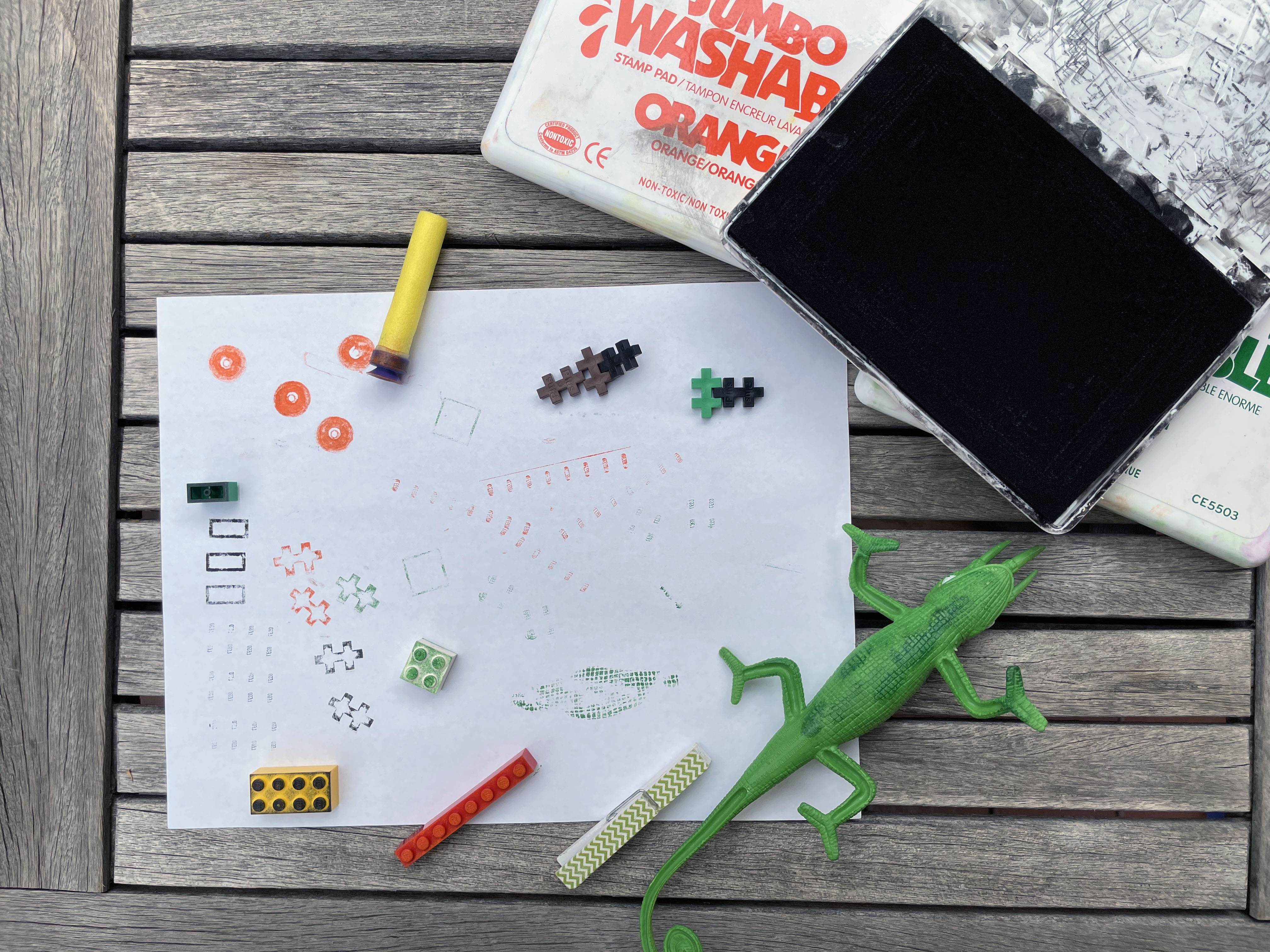 a toy lizard. legos and a Nerf dart lying on top of a paper after they have been used to make prints.