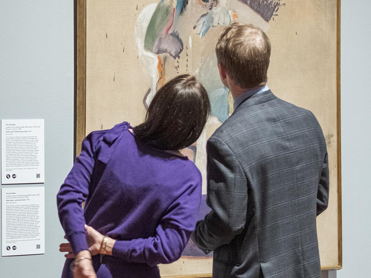 Two museum visitors look at a painting. 