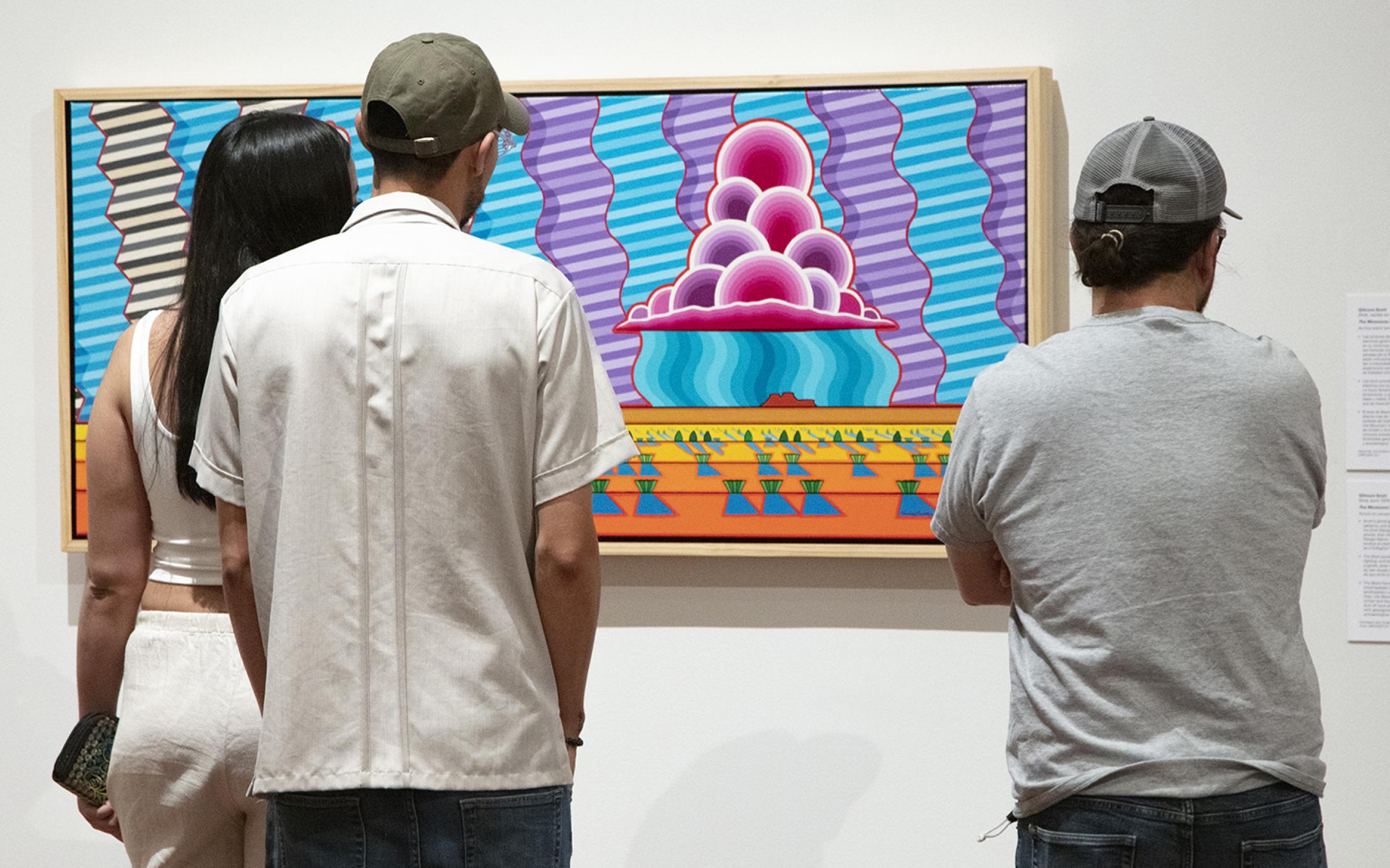 Three visitors look at a painting.