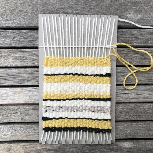 weaving on cardboard loom yellow, gray, white, and black yarn stripes