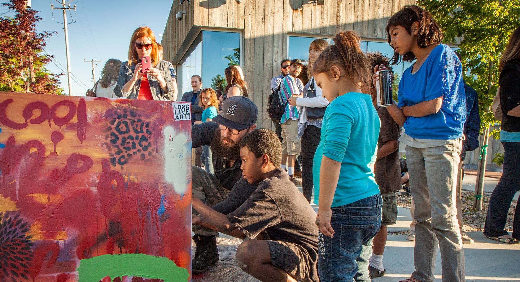 ACME Session spray painting activity with families. Artist and young boy work together to spray paint a colorful canvas