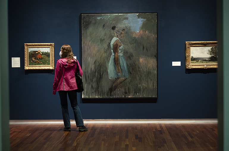 European gallery Spring 2021 a woman in a pink rain coat stands in the blue walled European galley looking at Lynette Yaidom-Boakye painting
