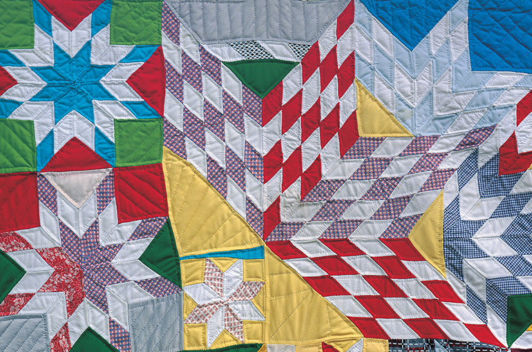 Cropped image of part of a quilt with a star pattern formed out of diamond pieces on fabric in yellow, white, purple and red. 