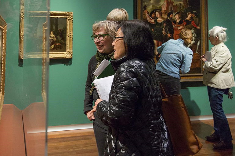 Docents in European Gallery Two women look and discuss at a painting under a vitrine in the UMFA European gallery
