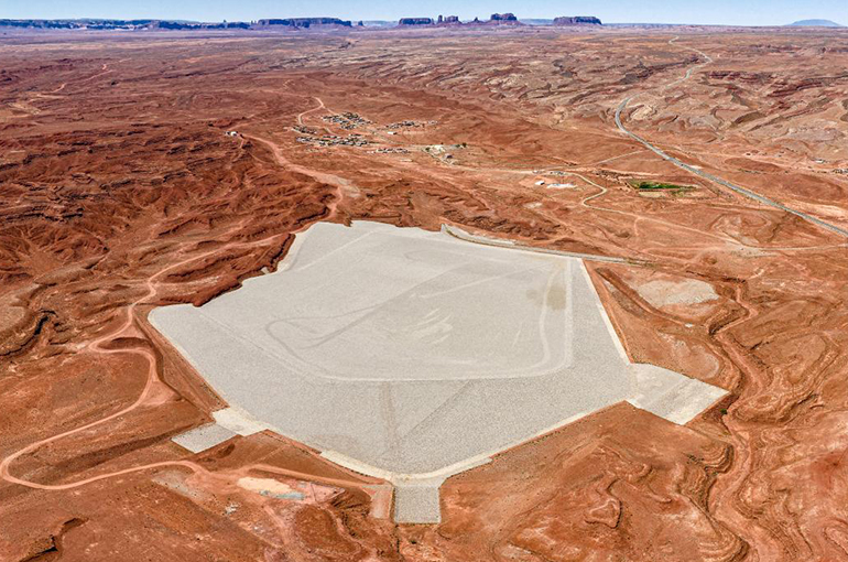 an arial landscape photo of an expanse of red dessert land with a large geometric five sided field of gray gravel at the center