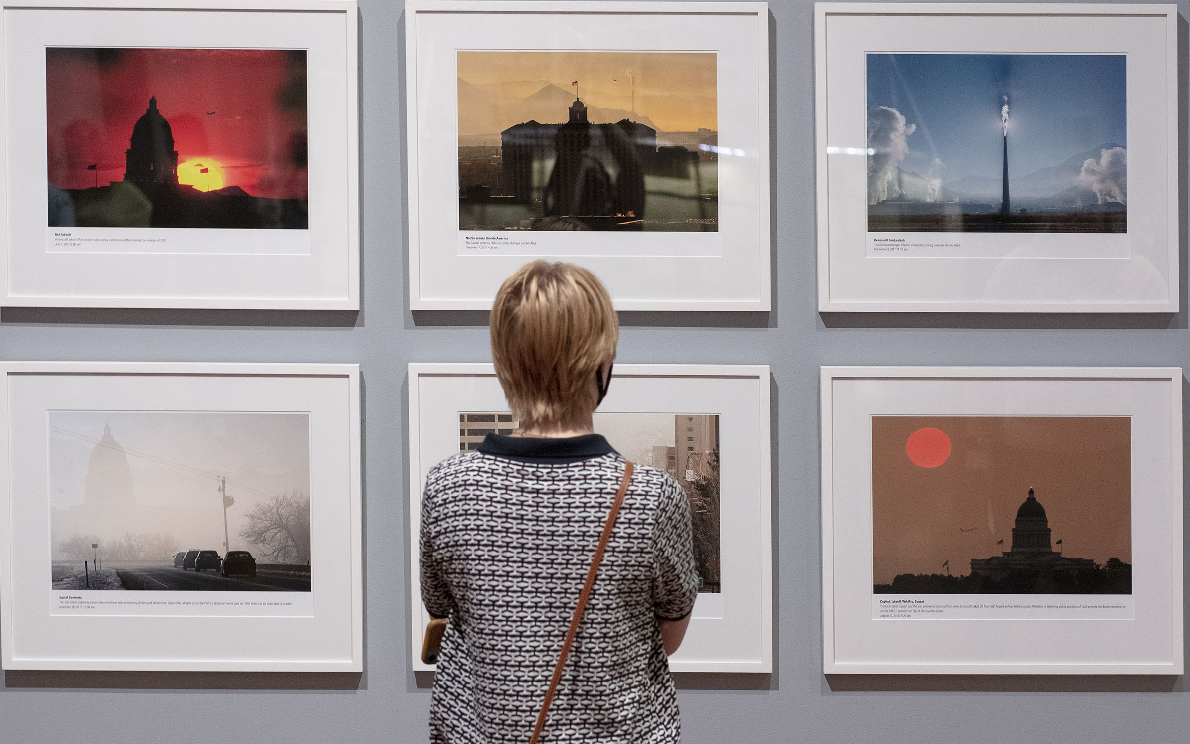 a museum visitor looks at six photographs of Salt Lake during bad air days, their back is to the camera