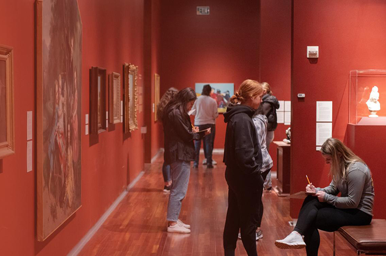 a group of young adults in the UMFA American Gallery looking at art.