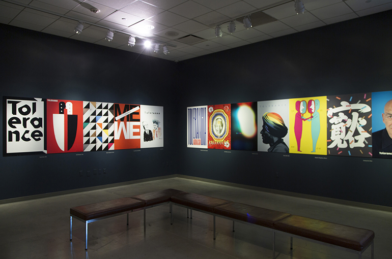 a large gallery room with black walls and a horizontal line of large colorful posters running down the center of the walls