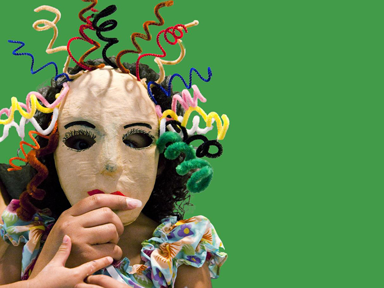 A child holds a mask with curly pipe cleaner hair to their face.