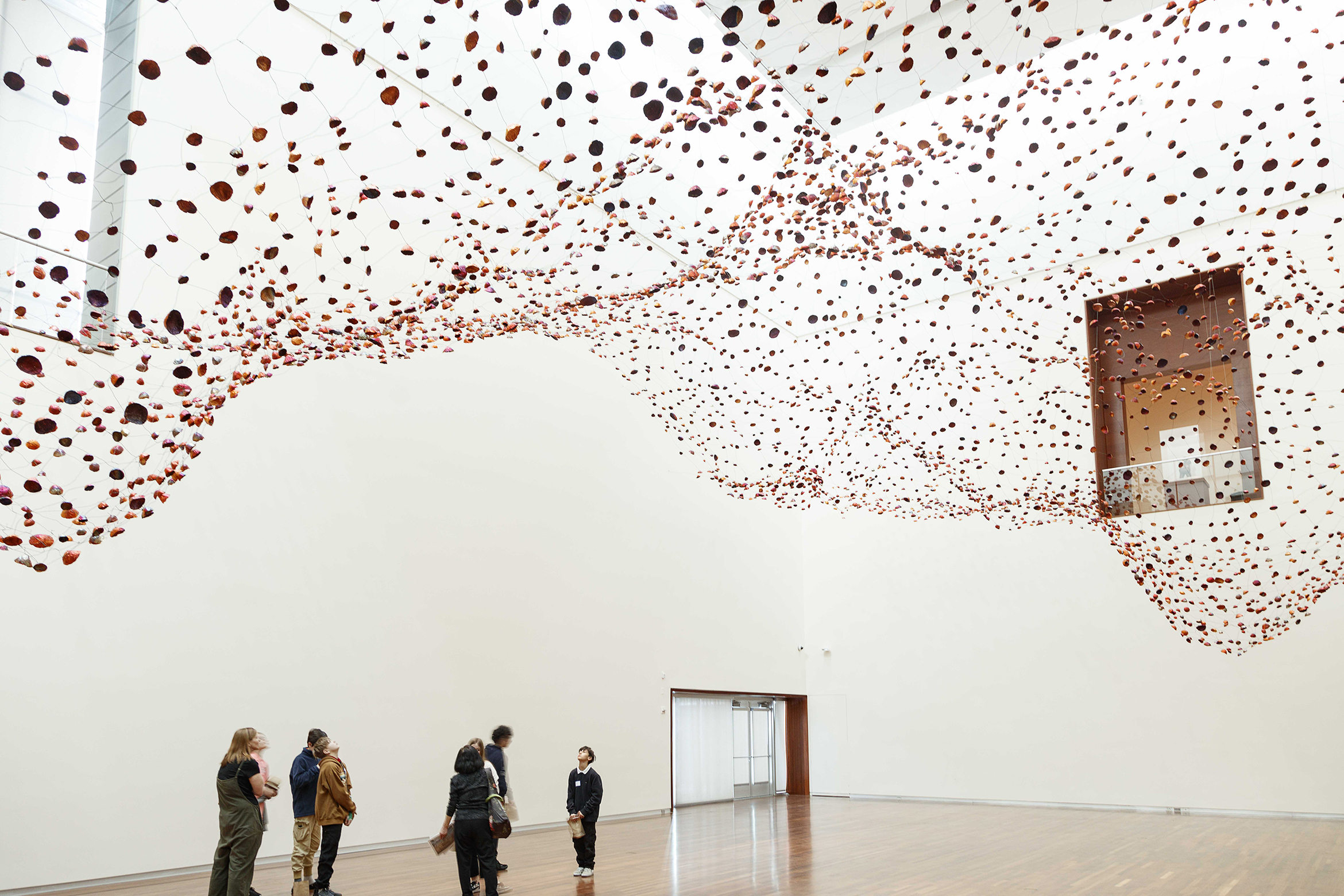 A group of people stand, looking up at thousands of copper foils shaped like rocks, suspended from the ceiling.