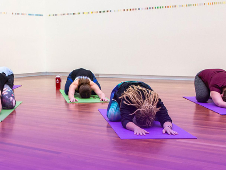 Several people sit in child's pose on yoga matts. 