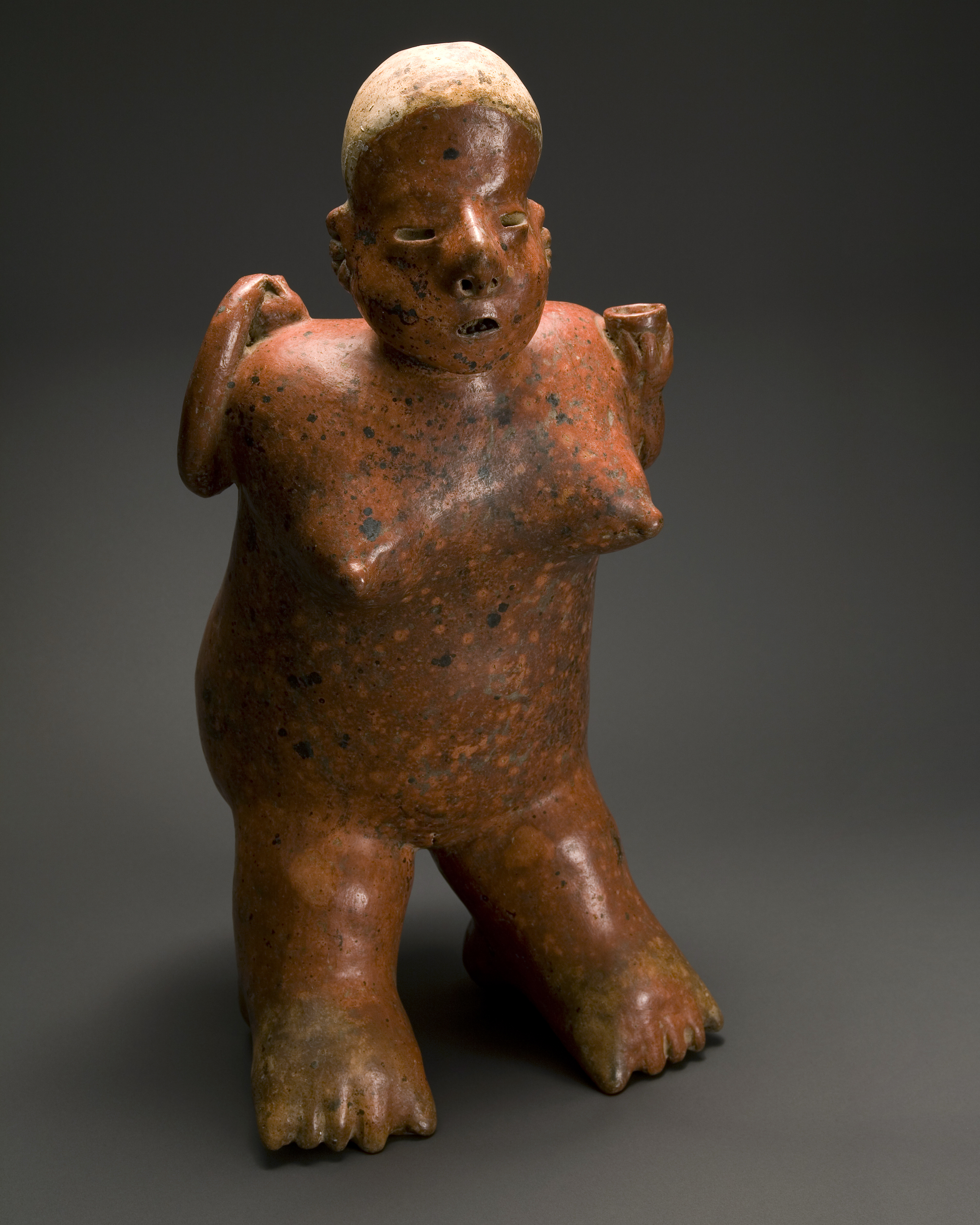 A red ceramic figure of a woman. She has short white hair and holds a small cup.