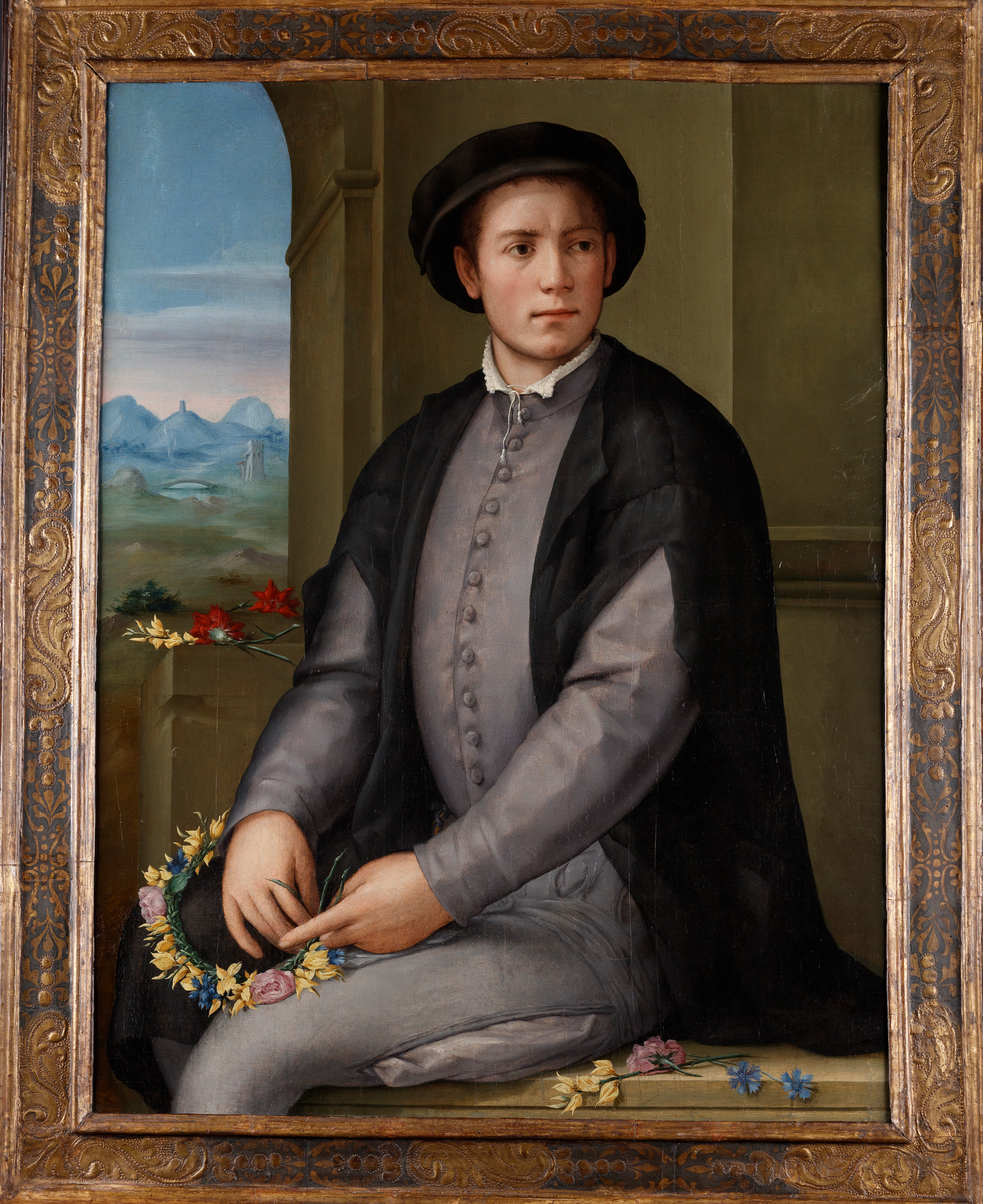 A portrait of a young white man. There is an unfinished flower wreath in his hands.