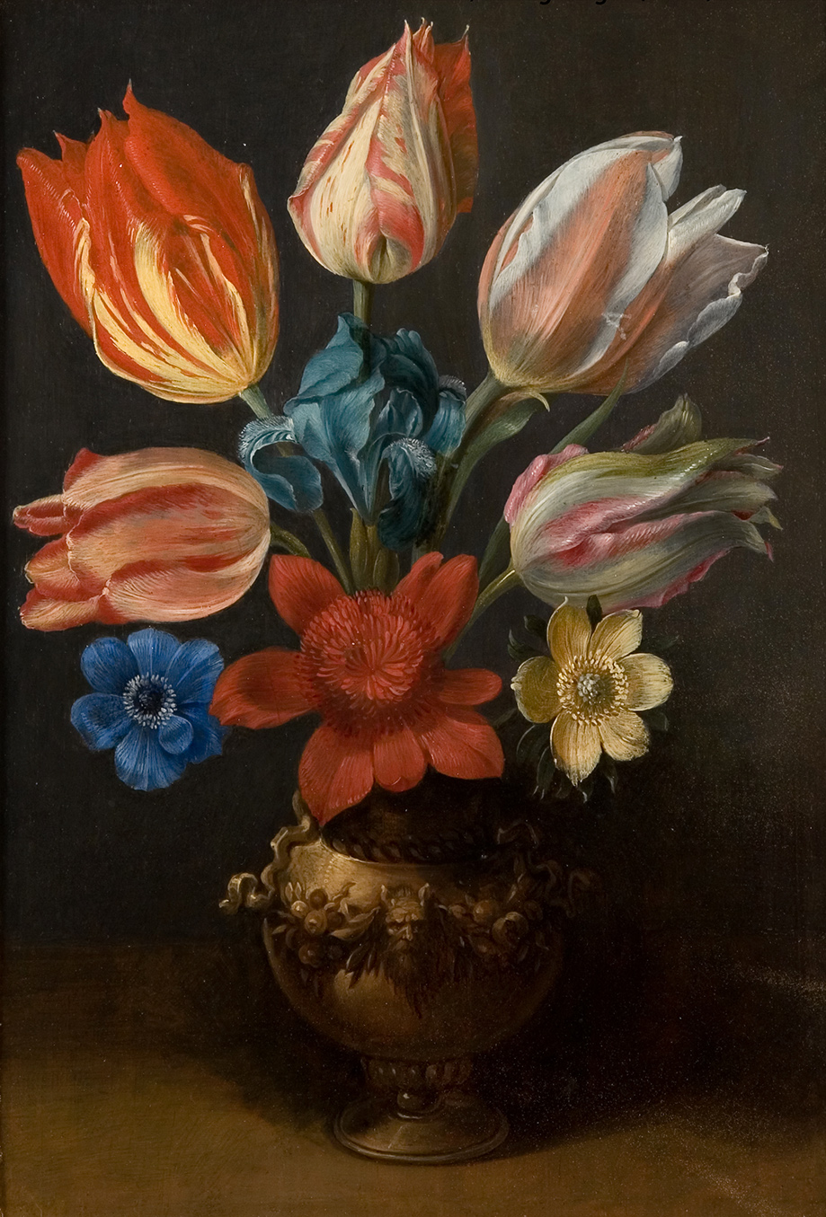 A pottery vase sits in the bottom center of the painting. It has applied sculptural flowers in a ring around the center with a sculpted face of a bearded man in the center. The vase holds five tulips, an iris, and three other flowers. The tulips are mostly oranges and pinks with stripes of yellow and white. The other flowers are blue, red and yellow.