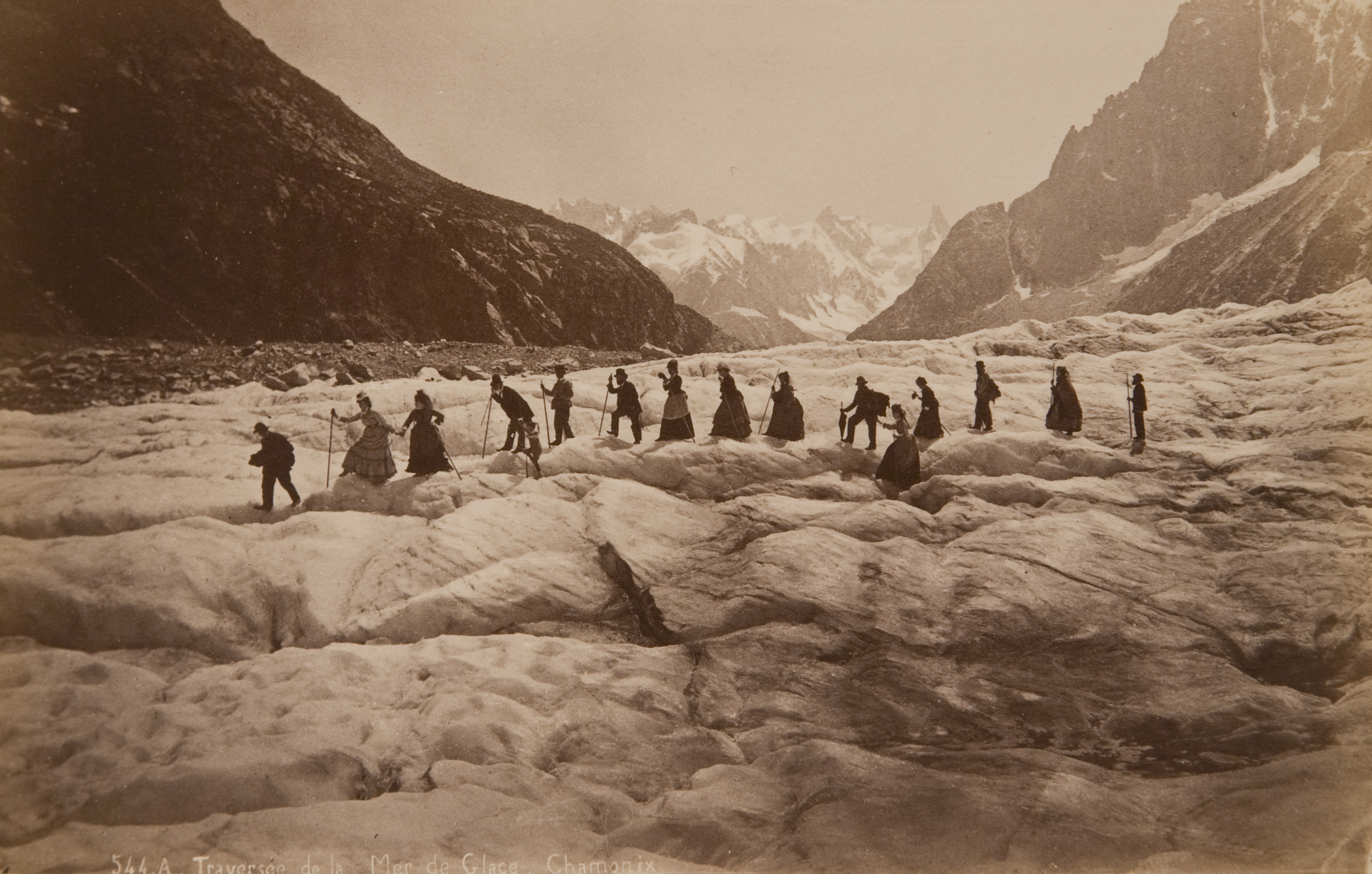 A black and white photograph of a group of people hiking across a glacier.