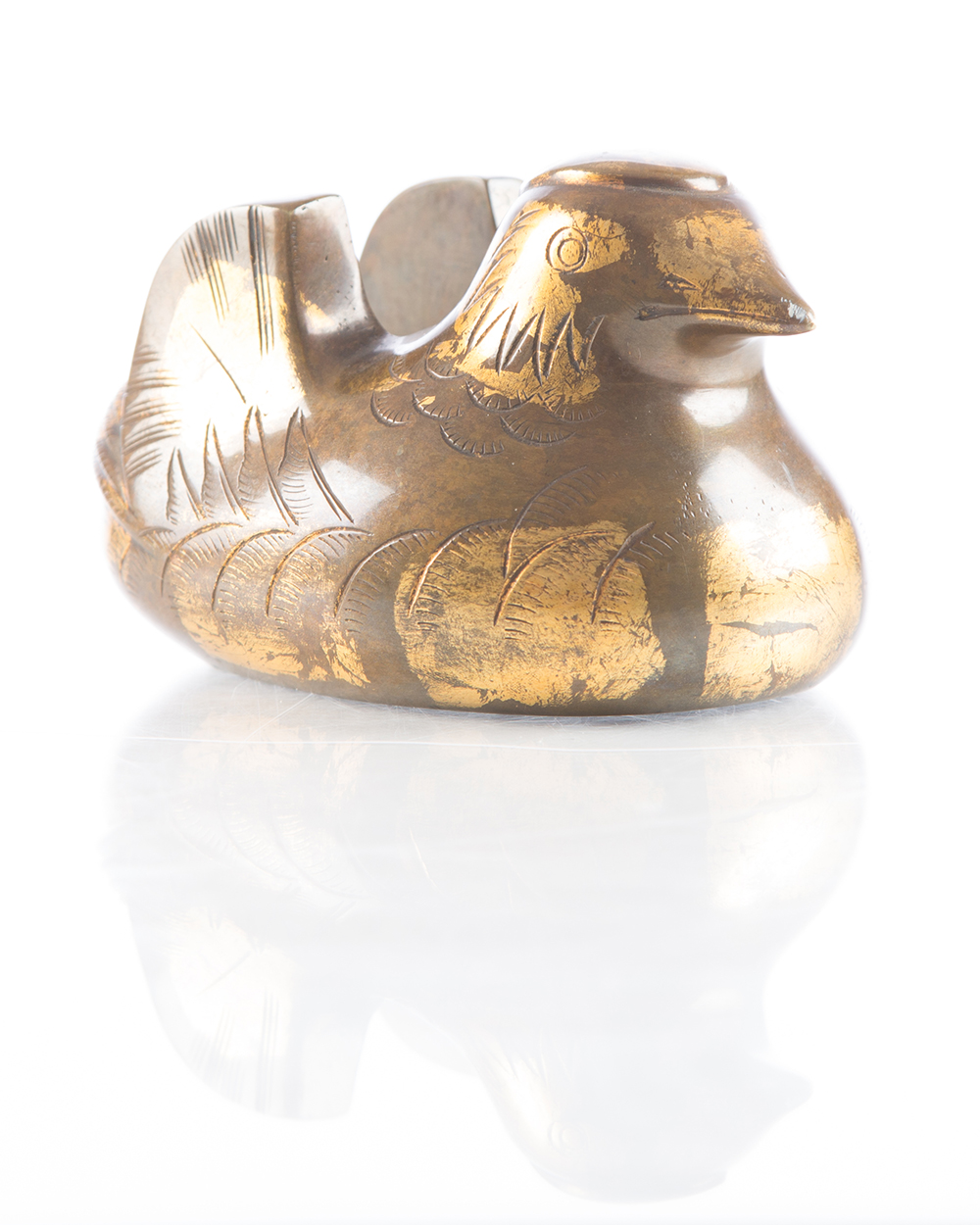 a 3” high brass sculpture of a bird with carved lines showing feathers, wings, and eyes. There are patches of gold leaf around the body and head of the bird. 