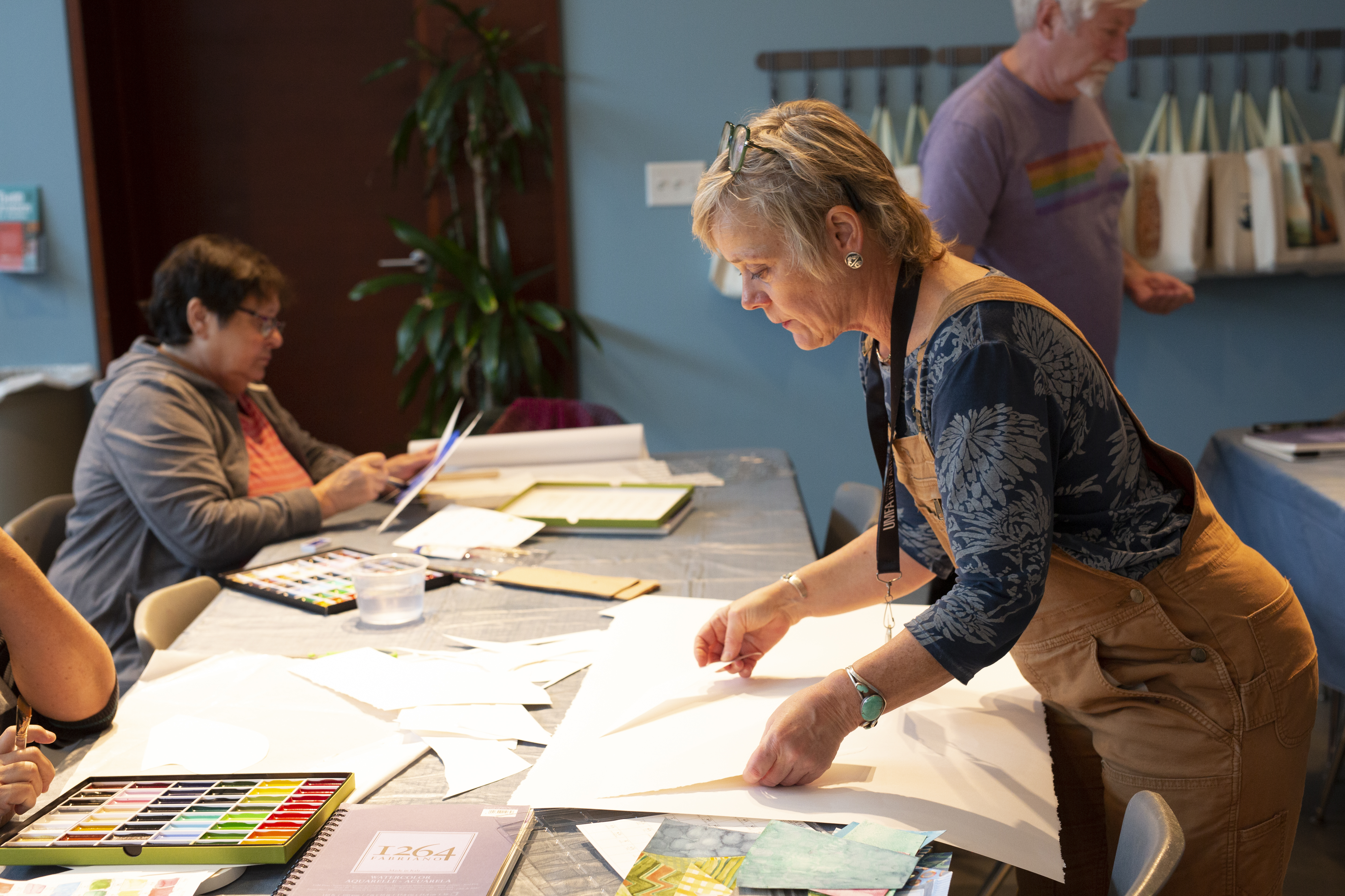 Laura Sharp Wilson bends over a table preparing art making supplies.