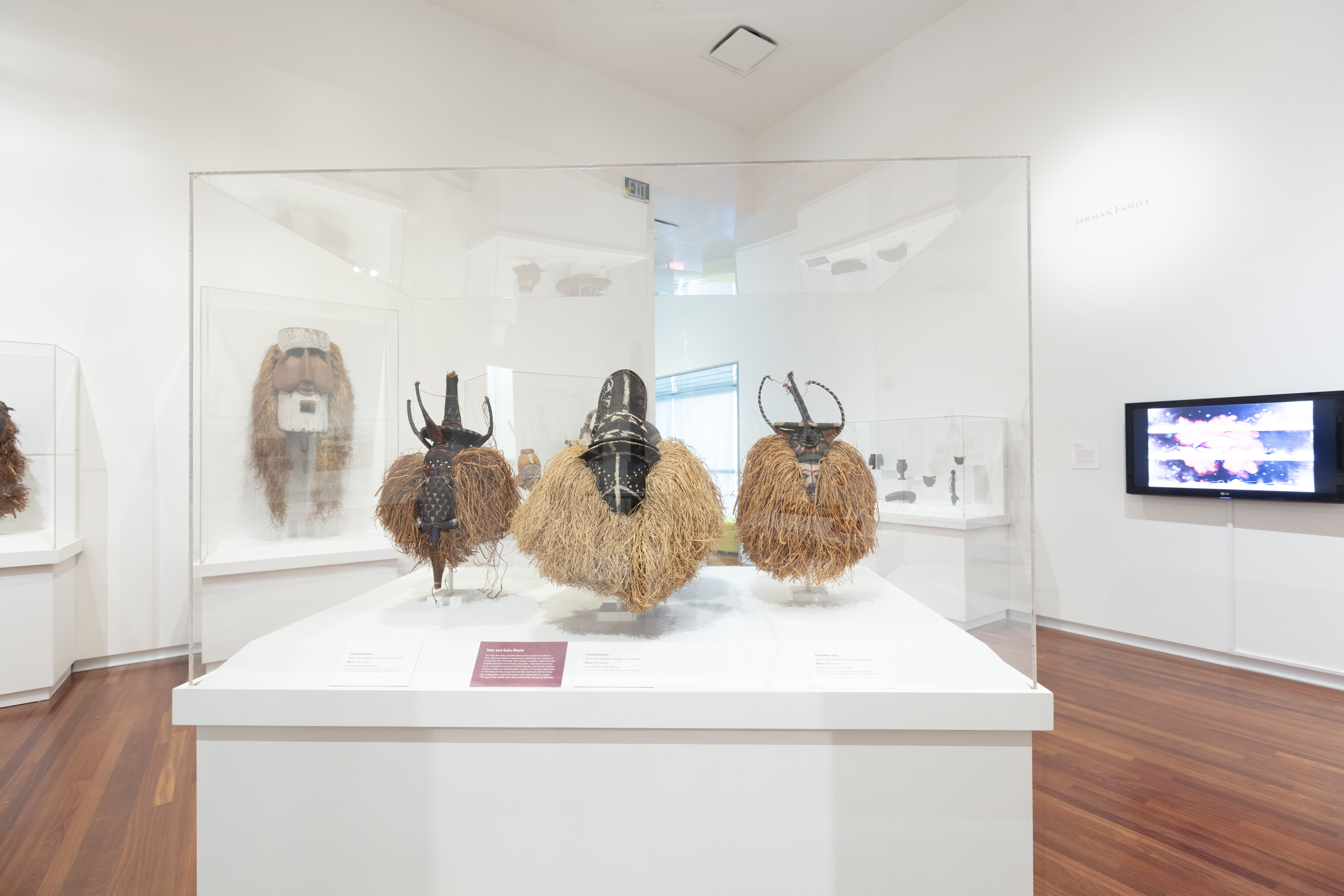 A gallery with three masks in a glass case and other objects on the walls around them.