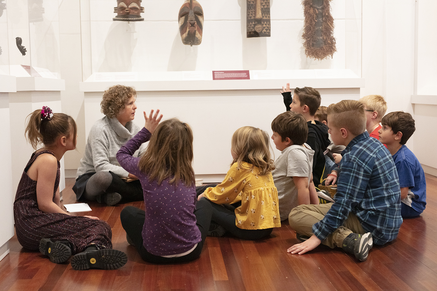 A group of young students sit on the floor and listen to a docent.