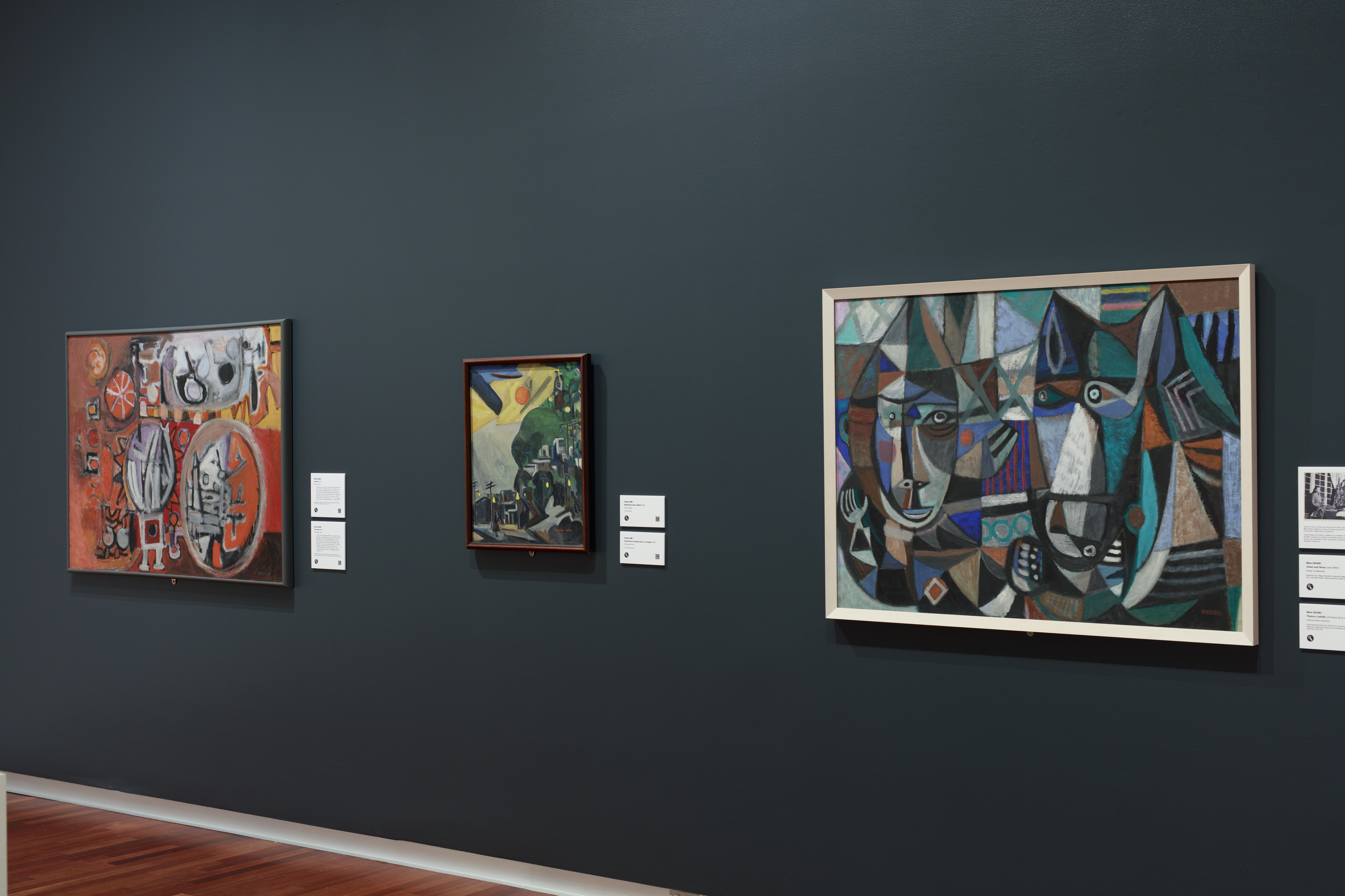 Gallery view of "Pictures of Belonging". Three paintings hang on the wall. A painting of a horse and a clown in blue, green, and orange is on the right.