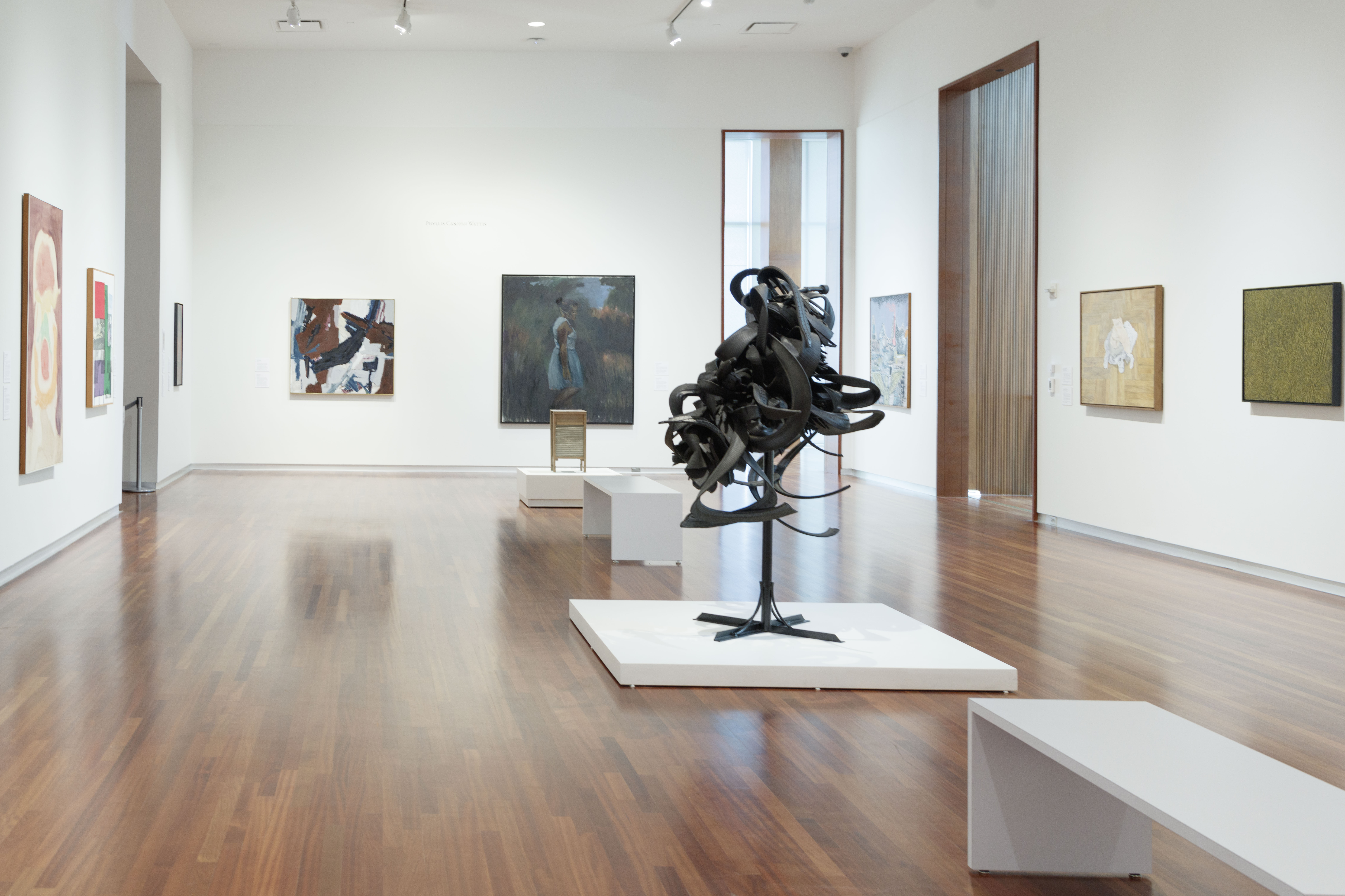 A gallery with an abstract sculpture at the center and colorful paintings on the walls.