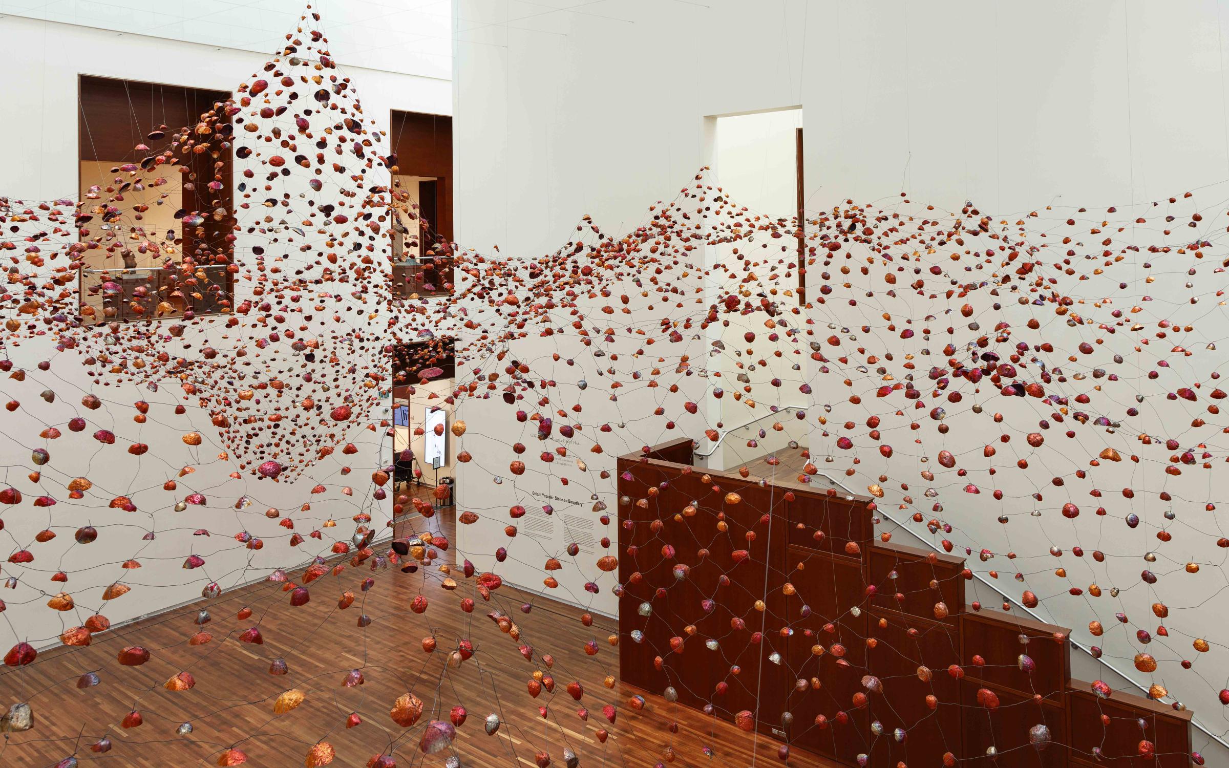 A photo of the UMFA Great Hall. The installation "Stone on Boundary" hangs from the ceiling creating a mountain and valley shapes out of a metal grid with copper bowls.