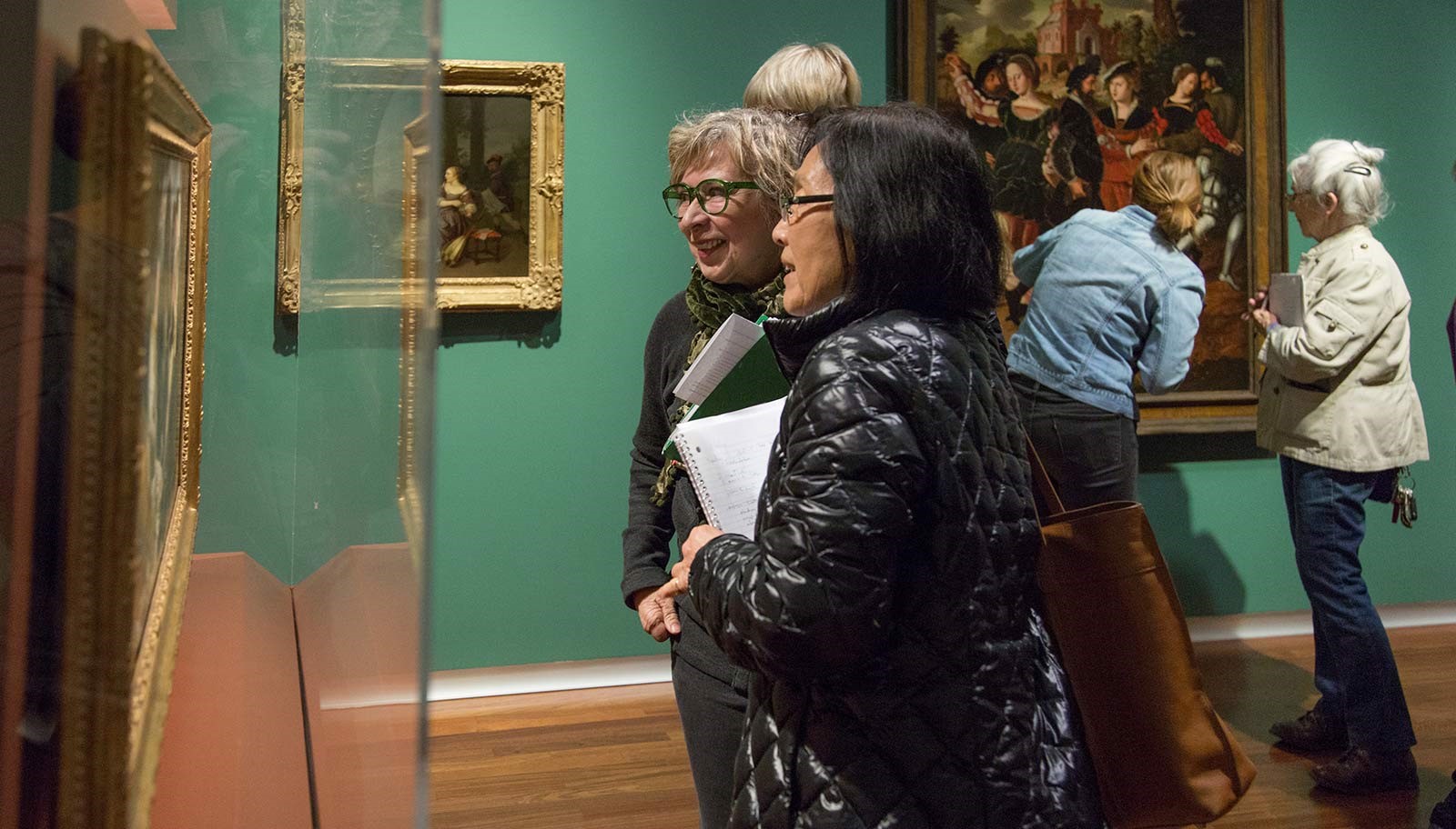 Two women look and discuss at a painting under a vitrine in the UMFA European gallery