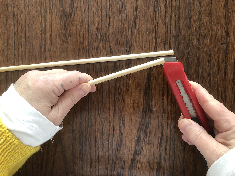 a person holding a dowel in the right hand and a razor knife in the left cutting a notch in the end of a dowel