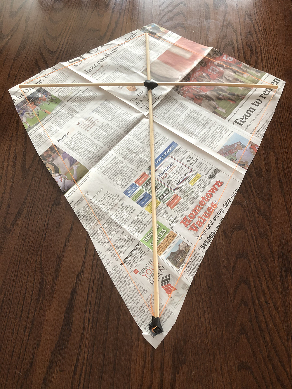 Kite frame on top of a piece of newspaper cut out to the same shape with extra edge to fold over the frame