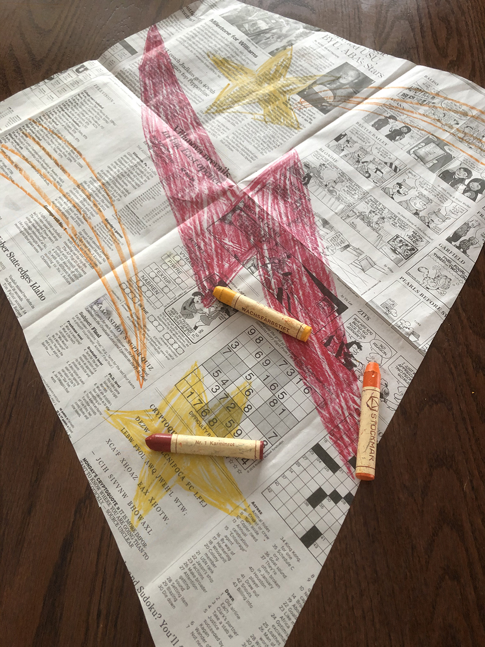 Newspaper kite with an orange lighting bolt colored on it in crayon