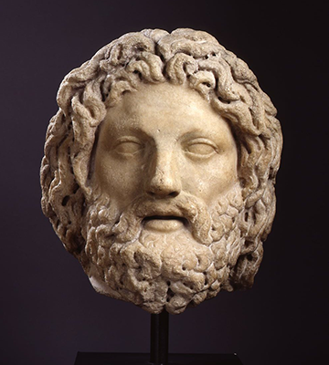 A marble statue of a mans head. He has long hair and a beard.