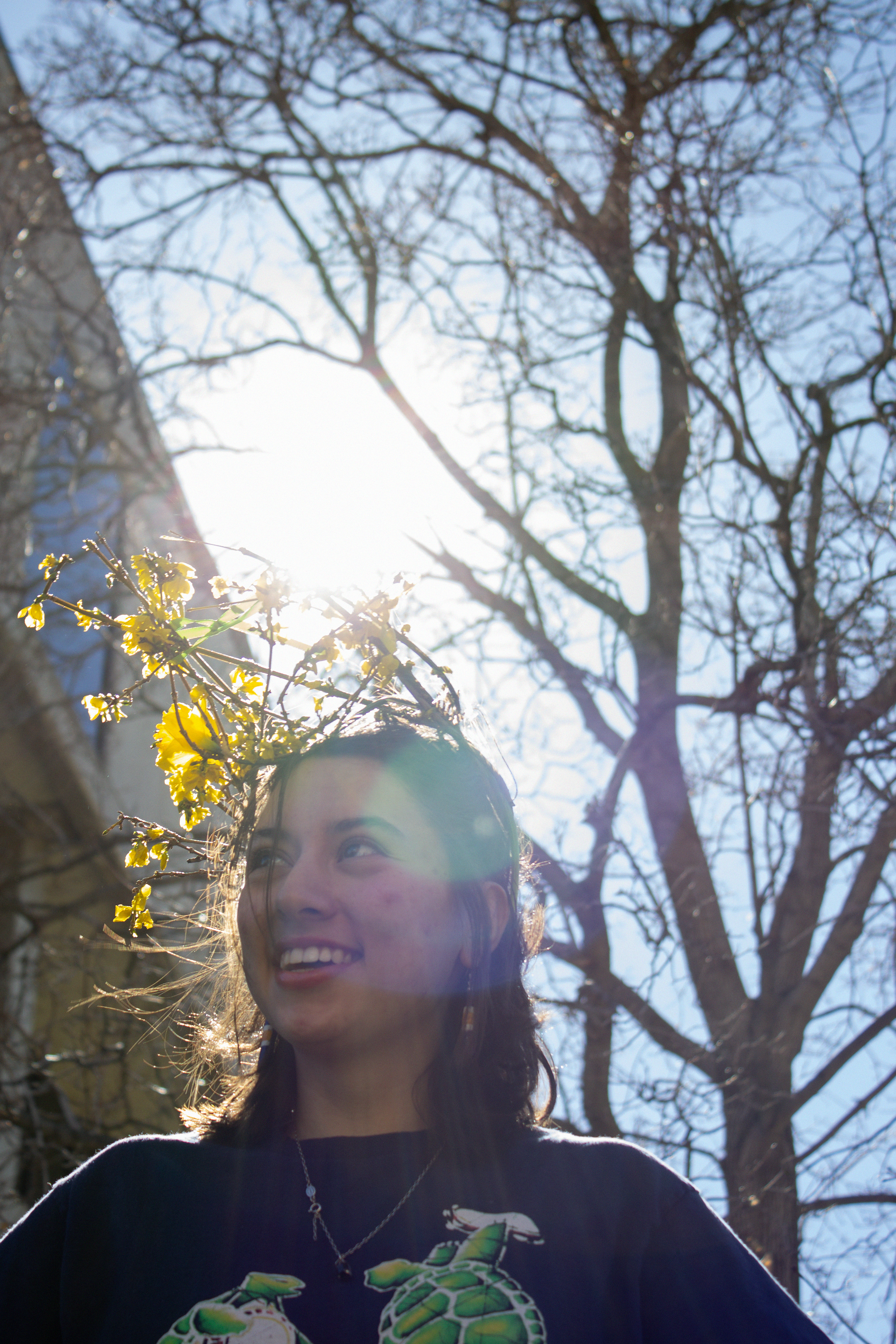 a portait of a white woman with dark hair, smiling outside in the sunlight in front of a tall tree.