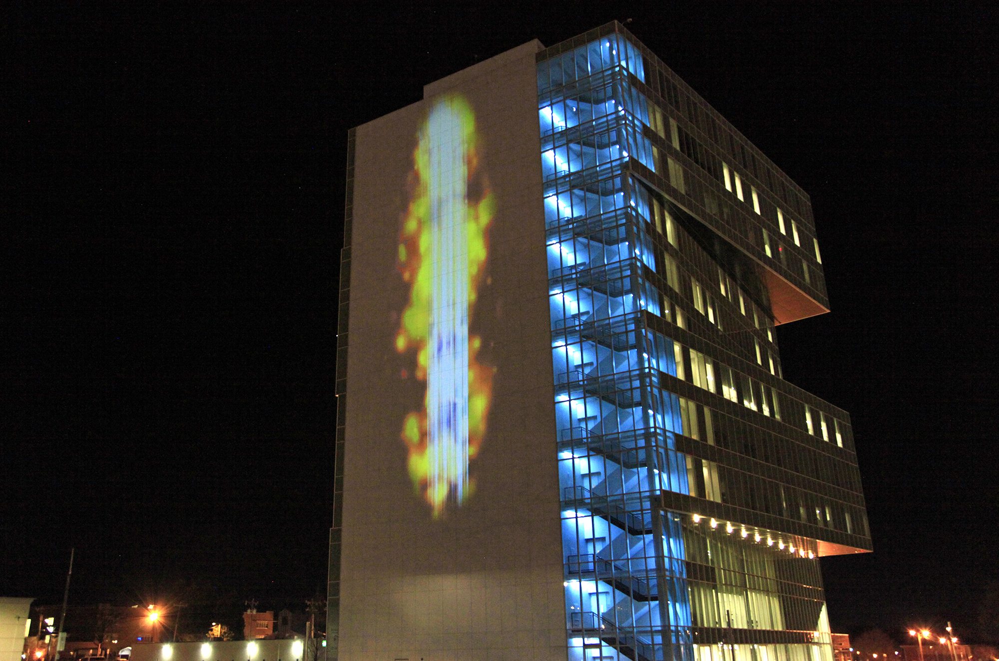 Andrea Polli, Particle Falls | City Center, UNC Charlotte 2016 | Blue light, occasionally interrupted by fire-colored spots representing air pollution, cascades down the side of a building.