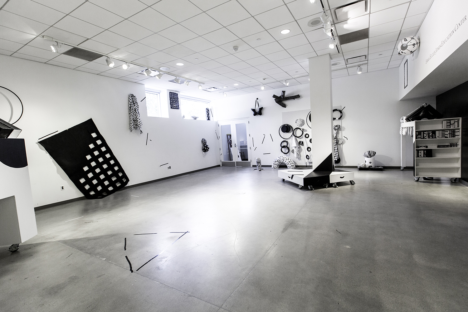 a large gallery room with a cement floor and white walls, there are black and white abstract sculptures scattered throughout the room