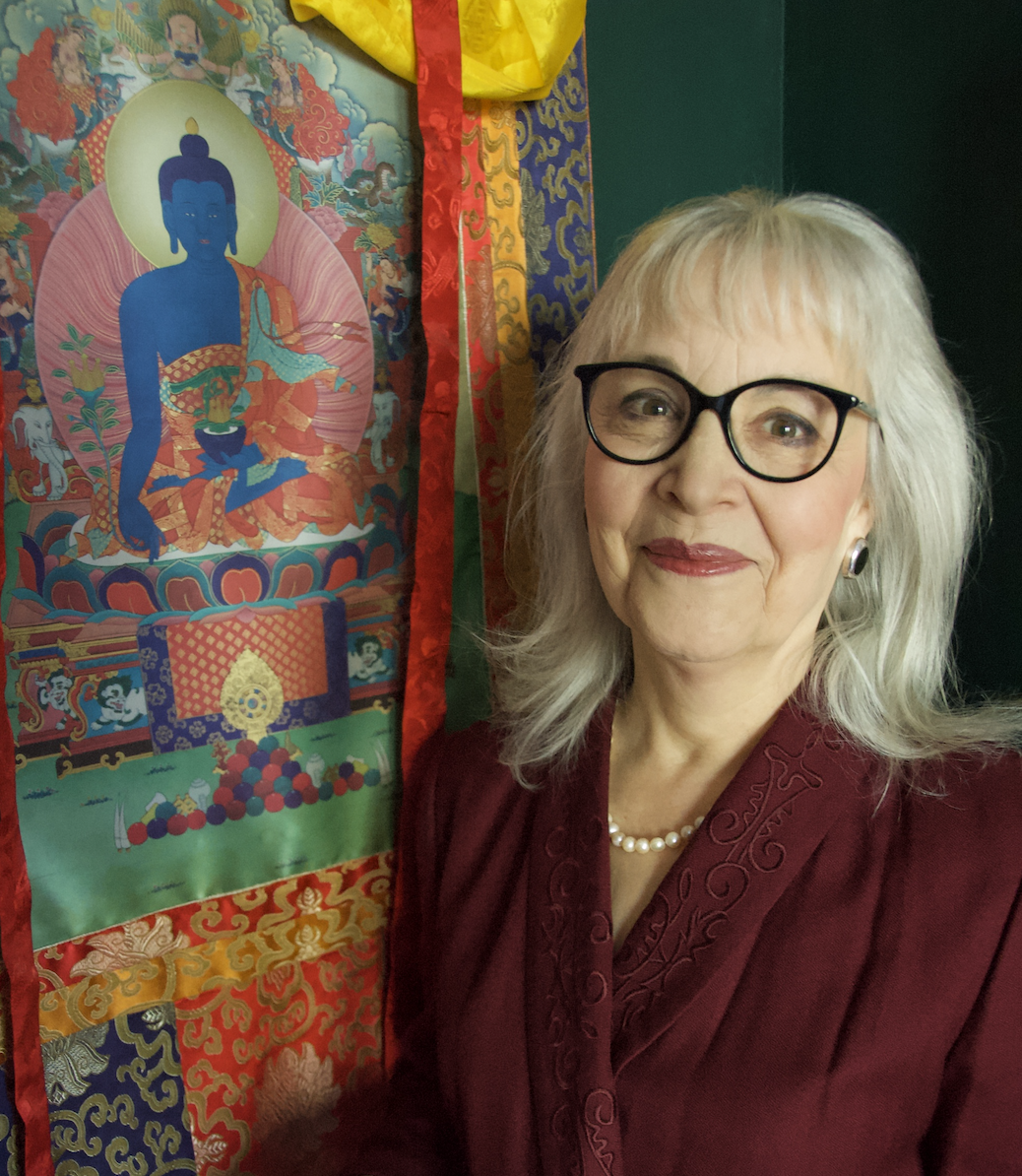 A photo of Ann Shaftel from the chest up. She is standing next to a colorful painting.