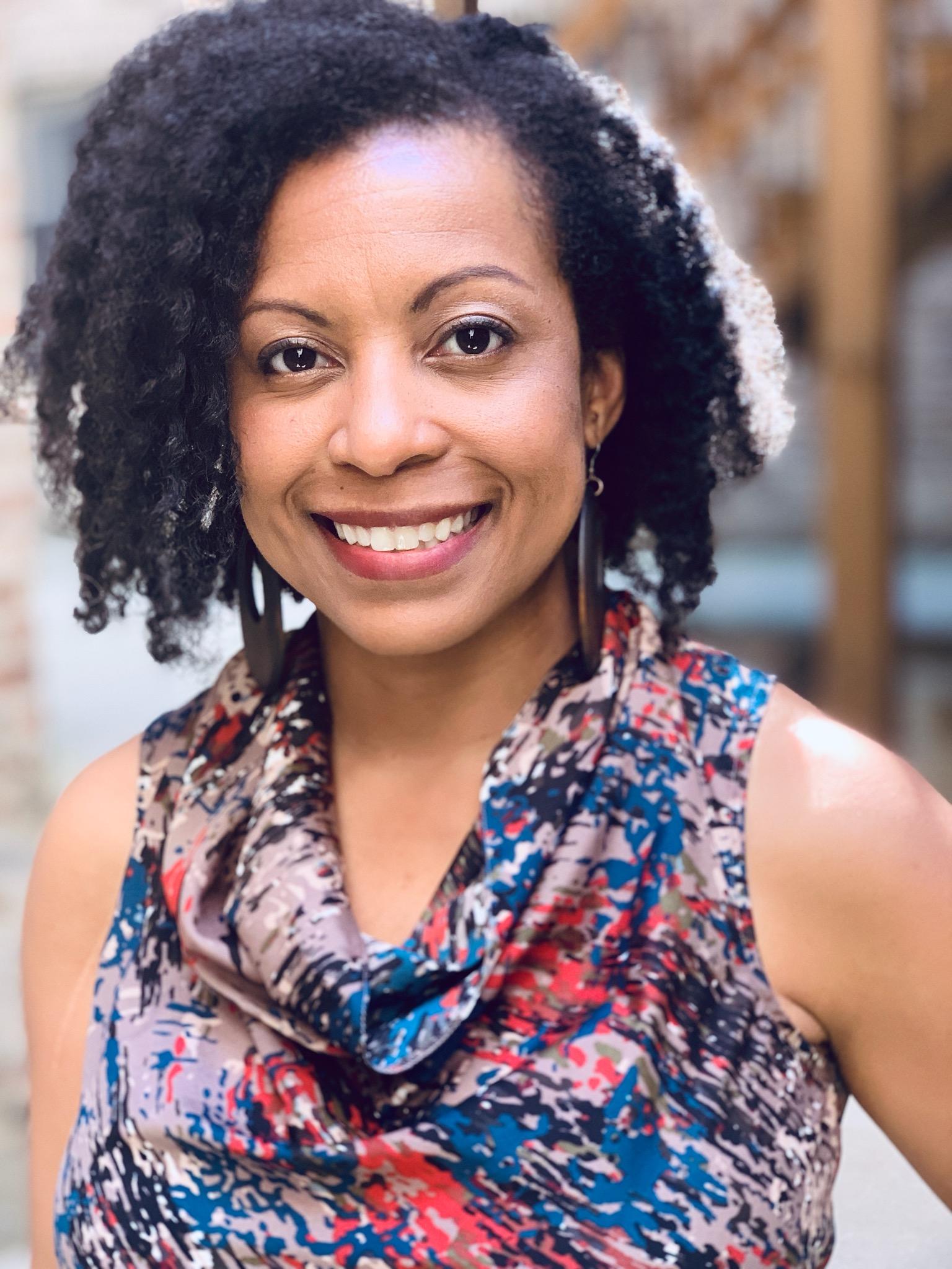 Crystal Rudds, a Black woman smiling with curly shoulder length hair.