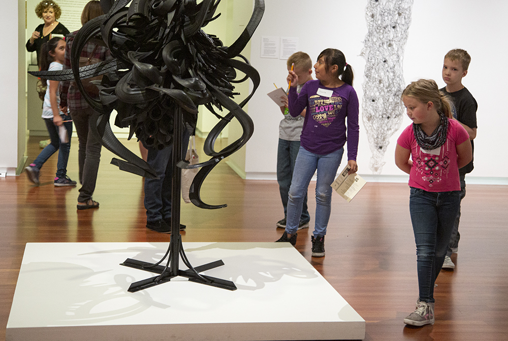 a group of school kids look at a sculpture made of cut and twisted tires 