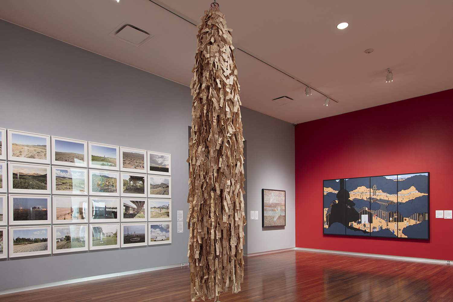 A large sculpture hanging from the gallery ceiling made of off-white fabric tags forming a ghostly shape 