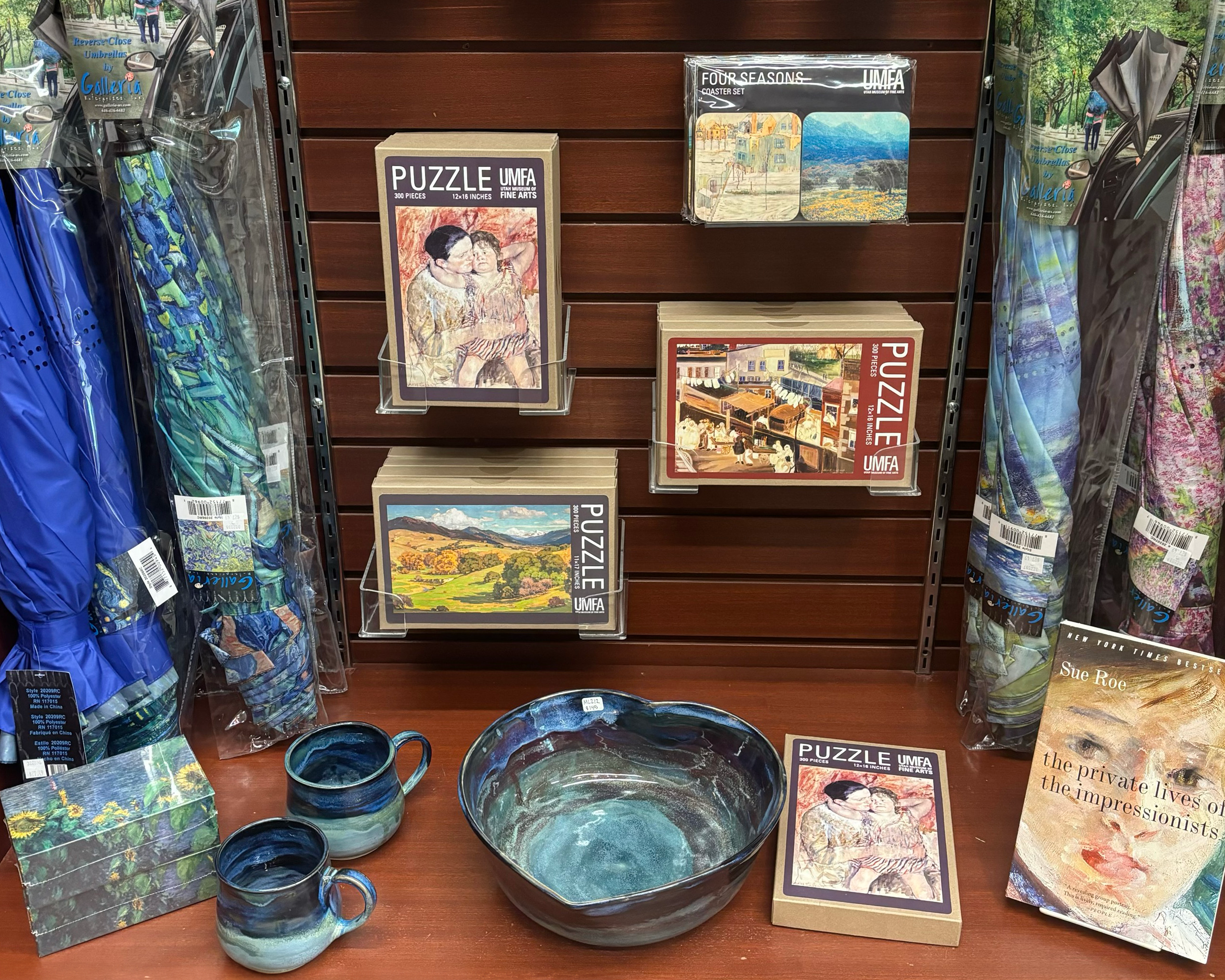 A display of items for sale including puzzles, umbrellas, magnets, and a book with impressionist paintings on them, and some glazed blue and green pottery pieces.