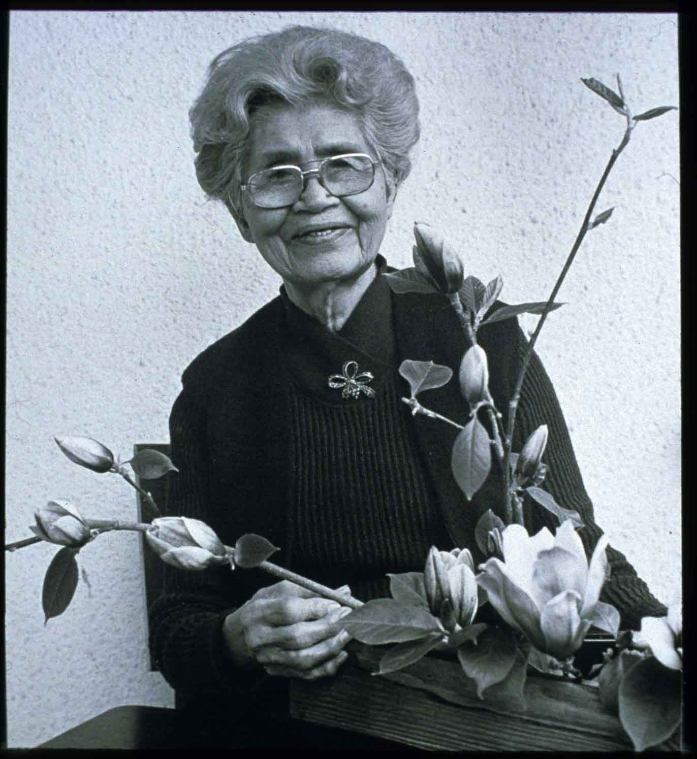 Haruko Obata smiles. A flower arrangement is in front of her. 