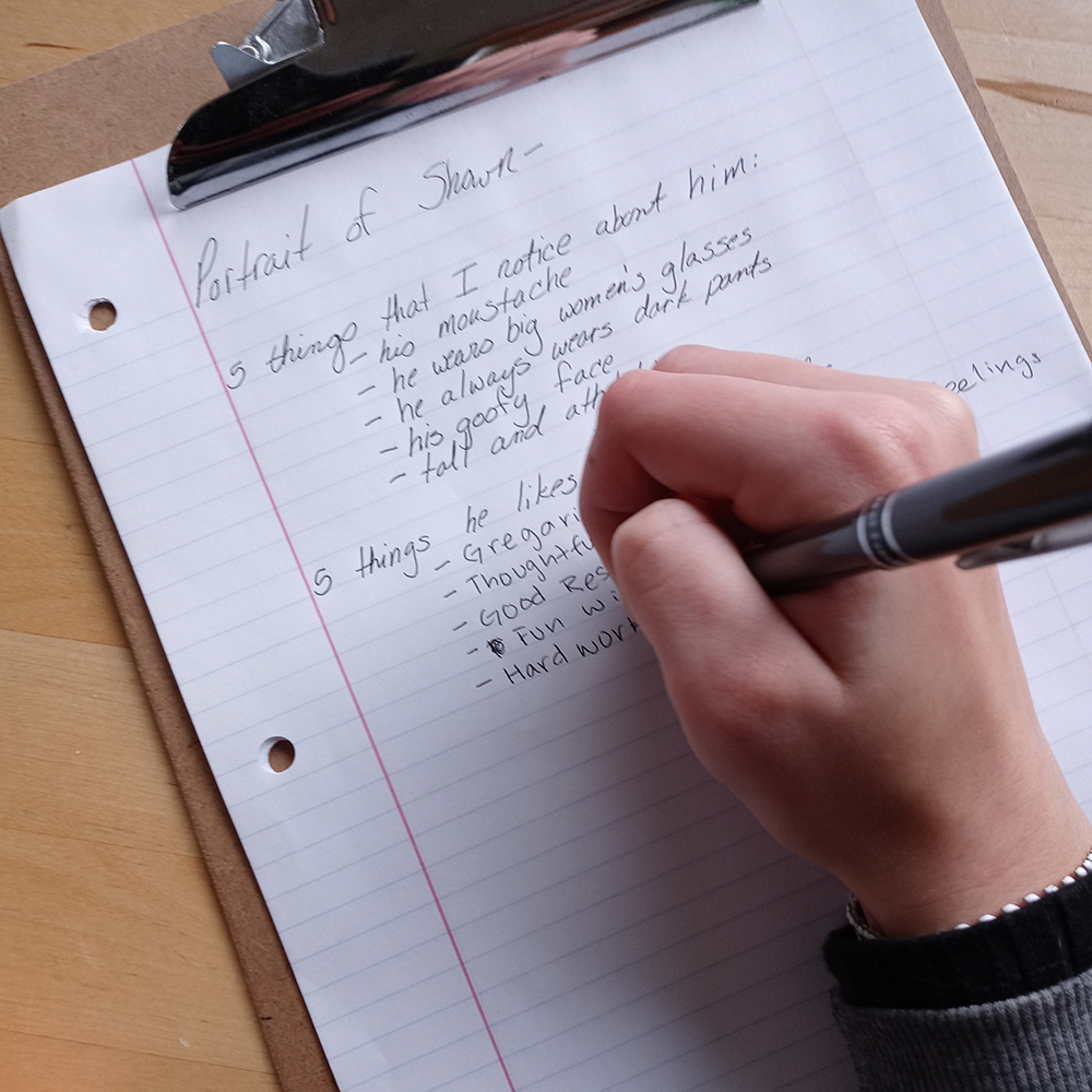 a piece of lined paper on a clip board with the hand of a young person with blue nail polish writing a list