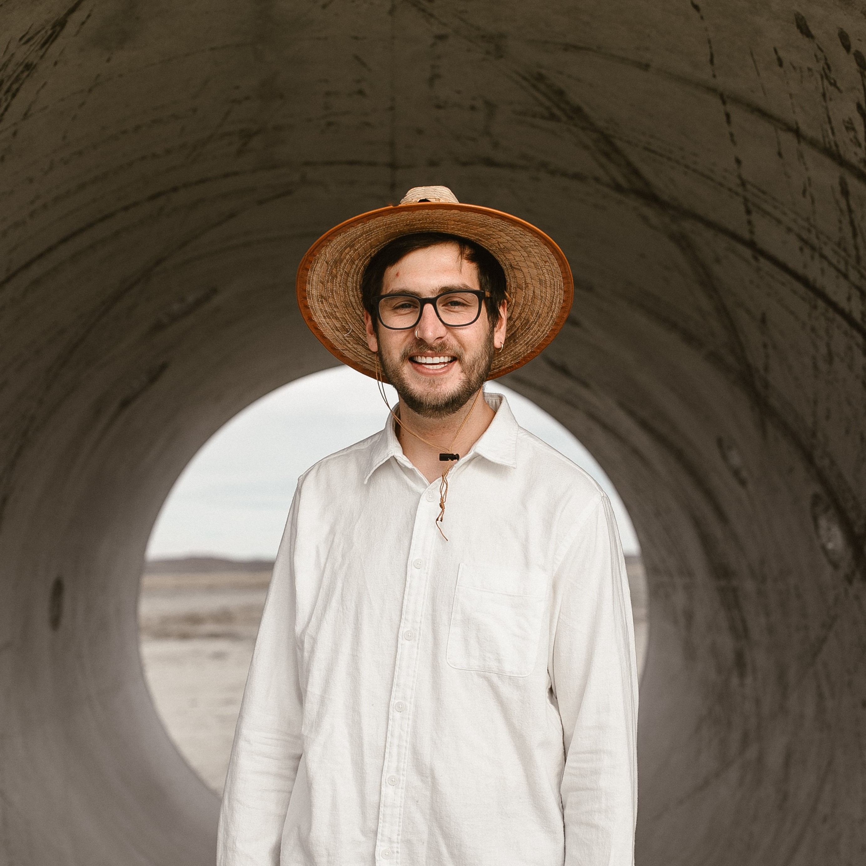 A tall man with fair skin wearing a hat in front of a Sun Tunnel.