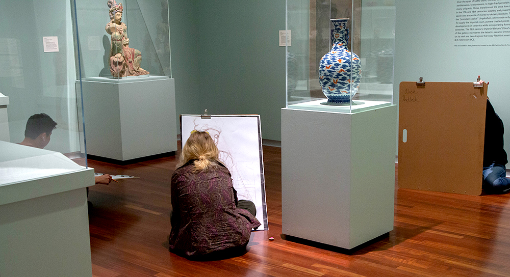 Three students draw in Asian gallery on large boards