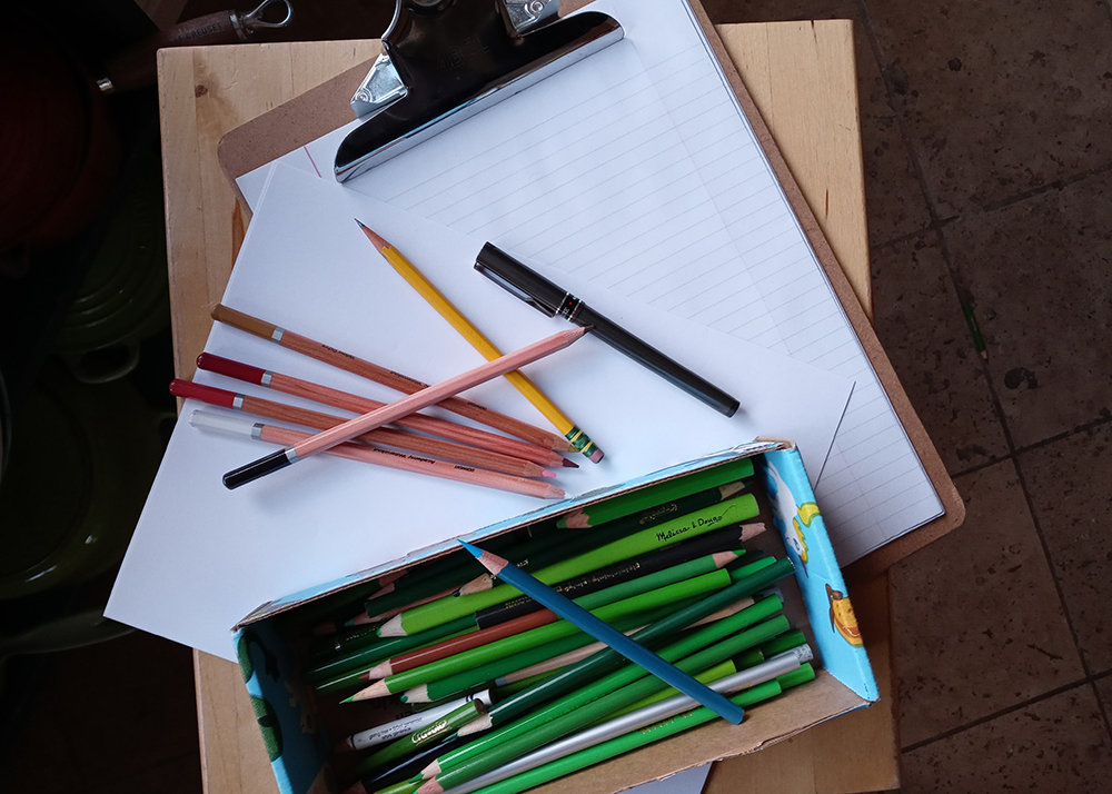 a clip board with lined paper a pile of pink and red pencils on the paper and a box with green pencils 