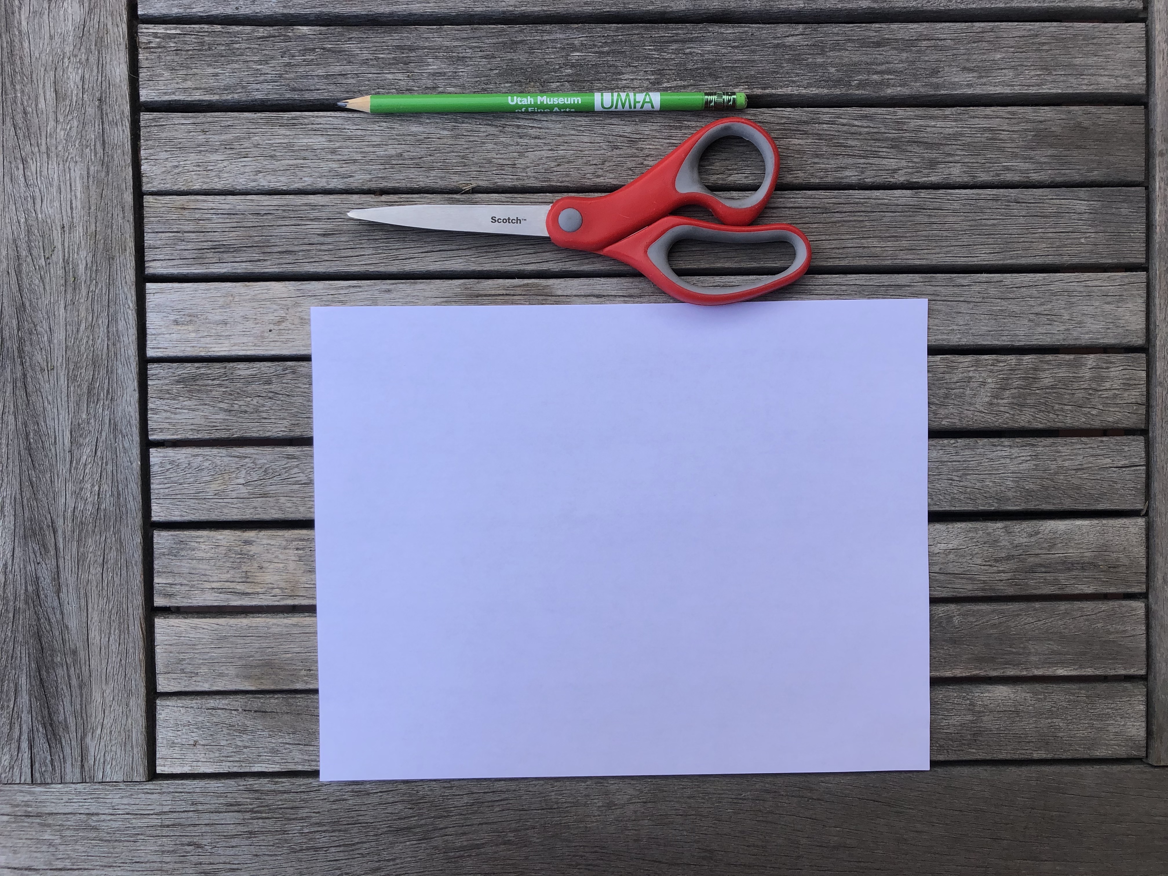 a piece of white paper, red scissors and a green pencil 
