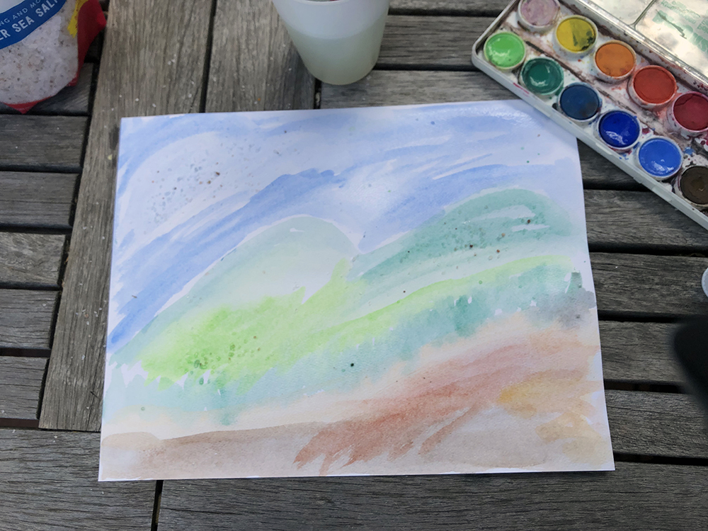 A table top with a watercolor paining of a landscape and a water color pallet 