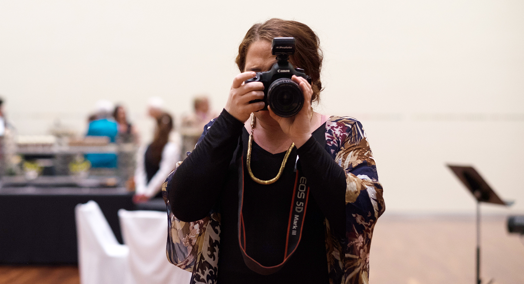 A woman has a camera in her hand, covering her face as she looks through the lens to take a photo.