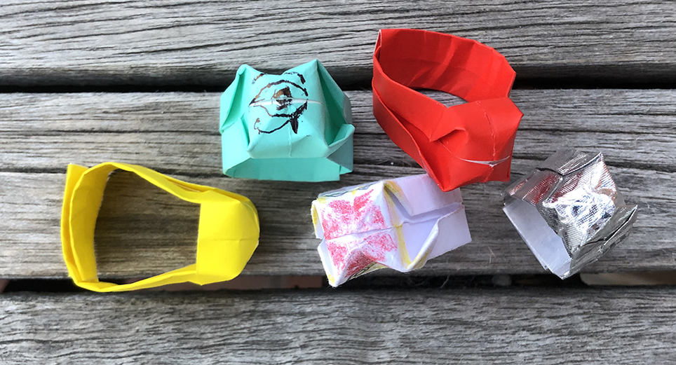 FIve paper rings on a wood table. One each in yellow, teal, red, silver, and white.