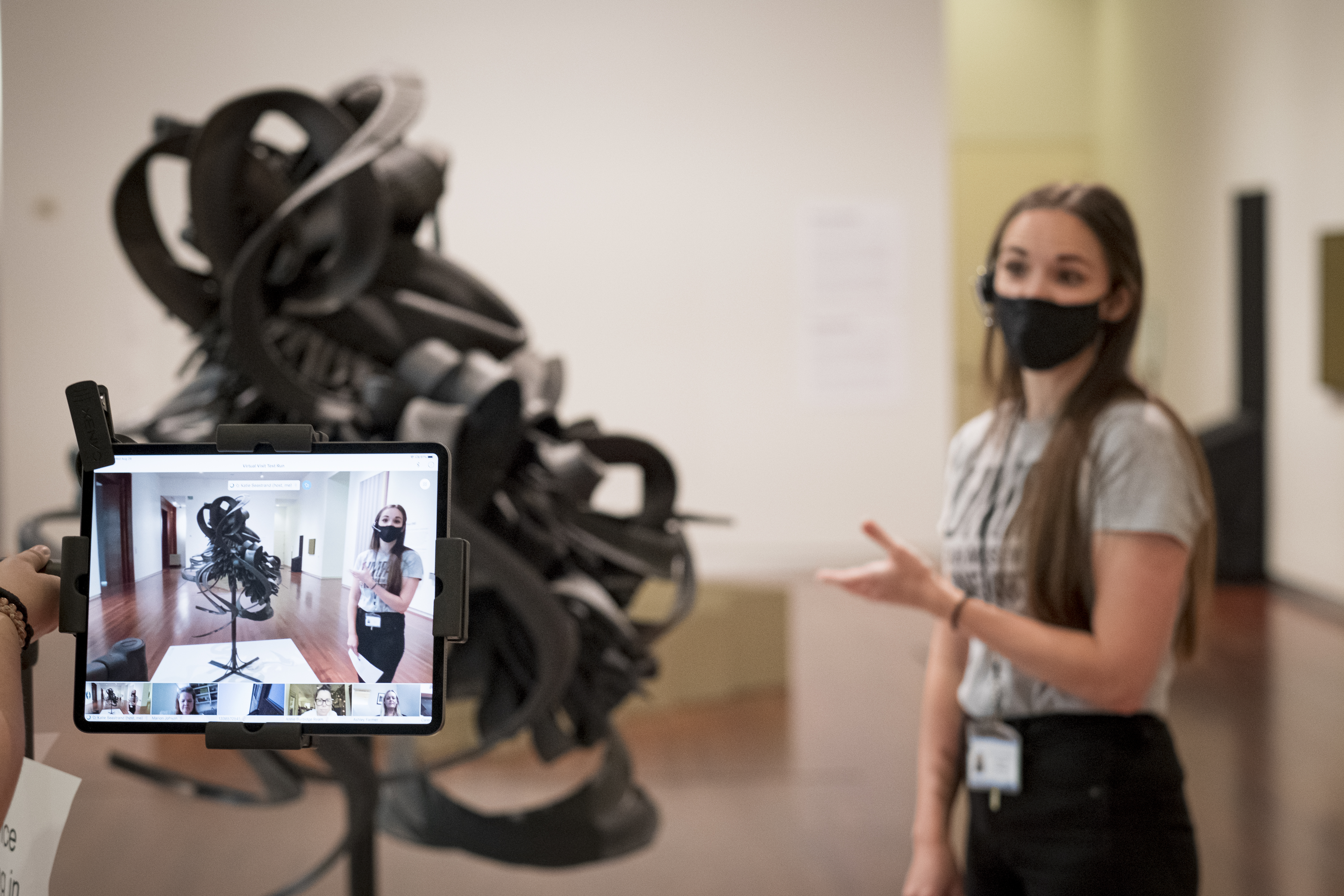 Katie Seastrand standing next to a sclupture made of tires teaching a class through an iPad 